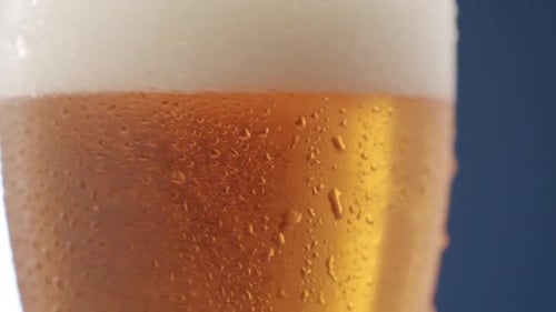 Nahaufnahme eines vollen Bierkrug mit viel Schaum und Tropfen auf Glas in Rotation