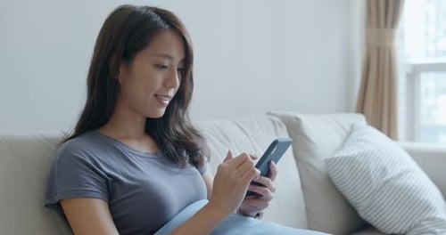 Woman Using Phone, Relaxing on Couch at Home