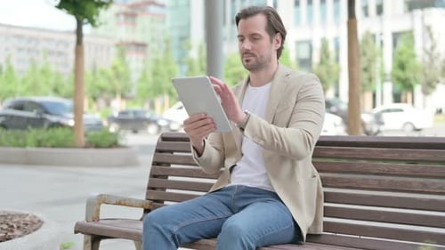 Man Using Tablet Sitting on Bench in City
