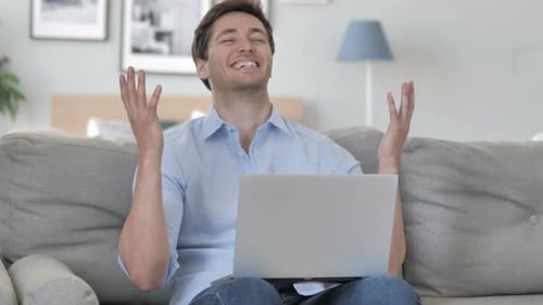 Man Reacts Positively to Laptop While Sitting on Couch