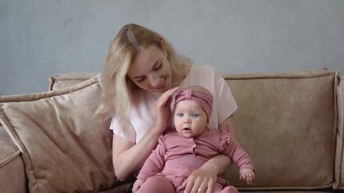 A Mother Holds Her Baby Daughter on Her Lap and Strokes the Baby's Cheek with a Smile