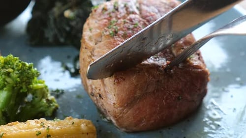 Close Up of Fresh Grilled Steak on Plate Cut with Fork and Knife on Plate