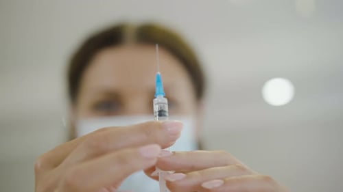 Close-up of Syringe with Covid-19 Vaccine in Female Hands with Blurred Caucasian Doctor at the