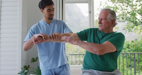 Slow motion of biracial male physiotherapist examining retired senior man's arm at nursing home