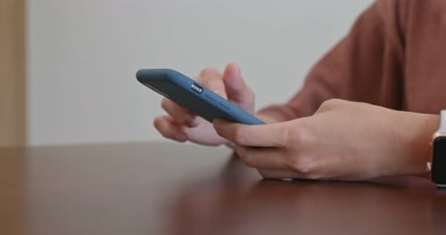 Hands Using Smartphone on Table Indoors