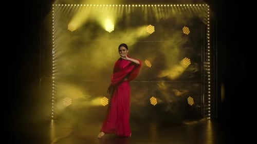 Une jeune fille danseuse dans un sari rouge, danse folklorique indienne, photographiée dans un studio sombre avec de la fumée et du jaune