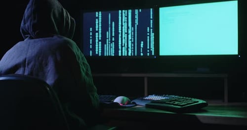 Un pirate informatique assis dans une pièce sombre piratant des systèmes de sécurité