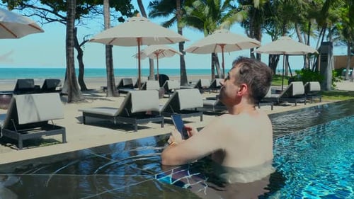 Young Man Use Smartphone Sunbathing Stand in Swimming Pool at Luxury Tropical Hotel Resort