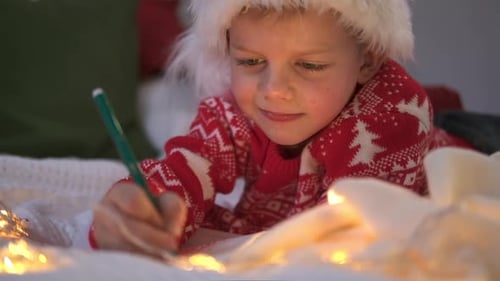 Festive Boy Writes Christmas List by Twinkling Lights