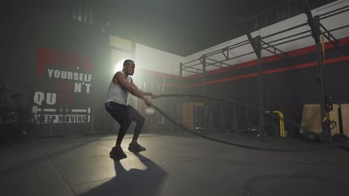 Black African American man doing battle ropes for cardio. Muscle strength training workout at gym