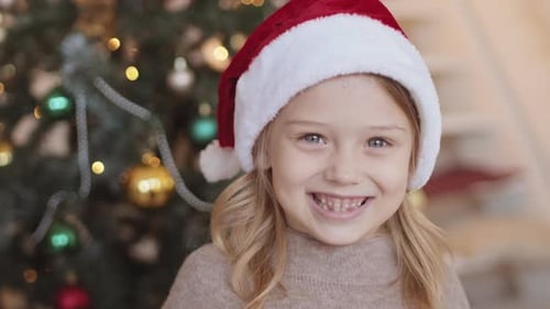 Smiling Girl Wearing Christmas Hat by Christmas Tree