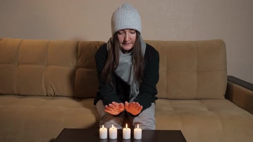 Frozen Woman Tries Heat Hands Over Burning Candles on Sofa