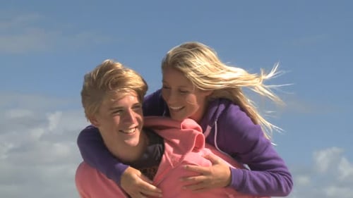 Young Woman Rides Piggyback on Man by Beach