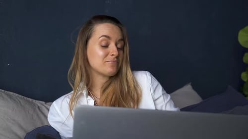 Frau sitzt auf dem Bett und hat Videoanruf über Laptop Akspb