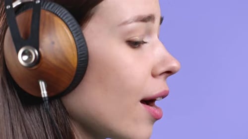 Pretty Woman Listening to Music Singing with Headphones on Violet Studio Background