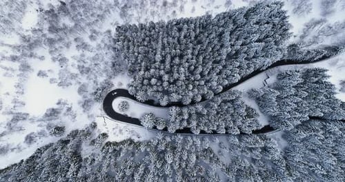 Overhead Aerial Top View Over Car Travelling on Hairpin Bend Turn Road in Mountain Winter Snow