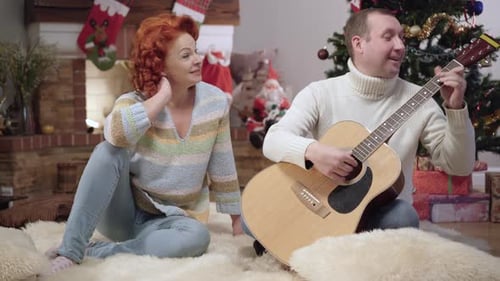 Man Plays Guitar for Woman at Christmas Time