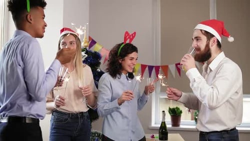 Grupo de trabalhadores de escritório felizes segurando luzes de Bengala e dançando usando chapéus de Natal e veados