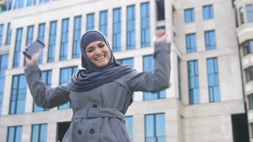 Excited Woman Looks at Phone in Urban Setting