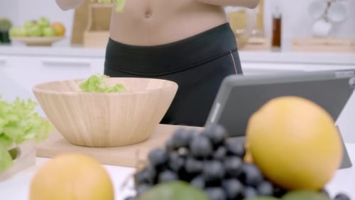 Woman Prepares Salad Using Tablet in Modern Kitchen