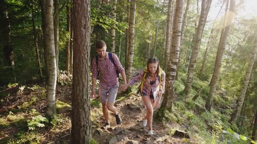 Young Happy Tourists with Backpacks Walk Along a Trail in the Forest