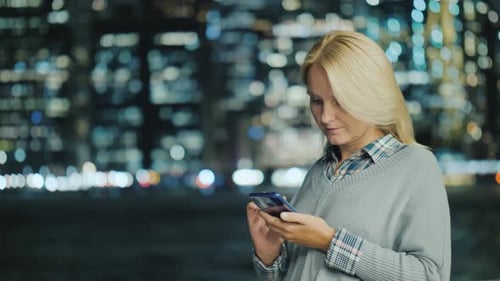 Young Woman with a Smartphone on the Background of the Lights of a Large Metropolis