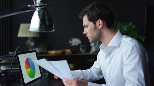 Geschäftsmann betrachtet Grafiken auf dem Laptop-Bildschirm. Manager arbeitet mit Papieren