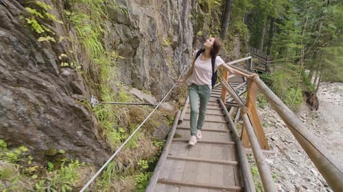 Frau mit Rucksack spaziert auf einer Holzbrücke in einem Bergwald