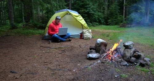 A Man Works on a Laptop in a Tourist Camp in a Beautiful Forest
