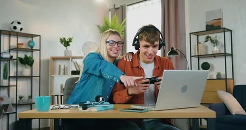 Joven con auriculares disfrutando de Vídeo en una computadora portátil cerca de apoyar a su novia sonri