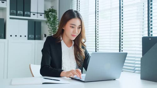 Asian beautiful smart business woman smile while work using laptop computer in office place.