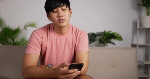 Young Man Uses Smartphone Indoors at Home