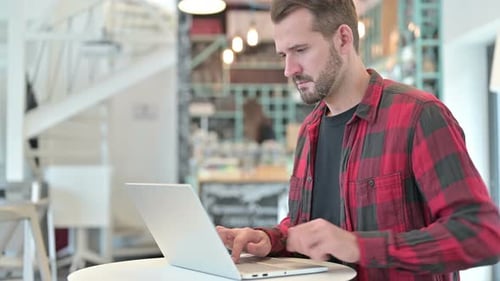 Young Man with Back Pain Using Laptop in Cafe