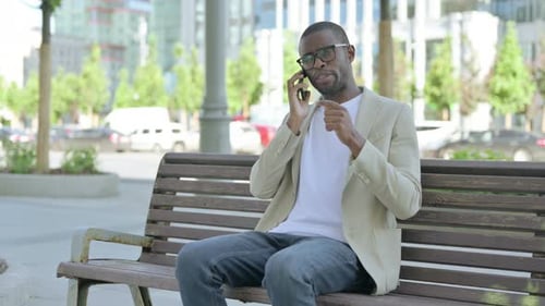 African Man Talking on Phone While Sitting Outdoor on Bench