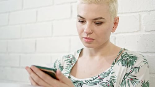 Close Up Pretty Blonde Woman with Short Hair Cut Sits on Bed in Morning in Greenwhite Pajamas and