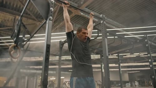 A Strong Male Athlete Makes a Way Out By Force on a Horizontal Bar in a Gym