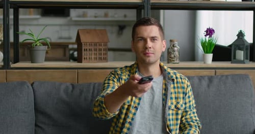 Young Is Sitting on a Sofa and Changing TV Channels