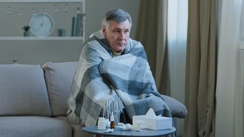 Man Wrapped in Blanket Feeling Ill on Couch