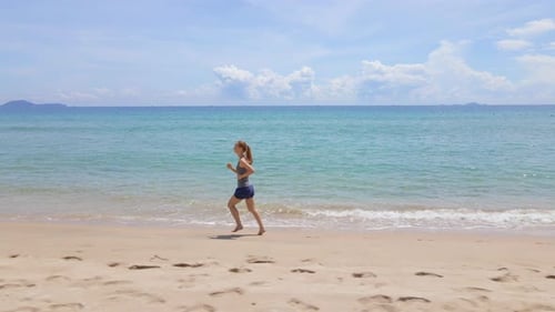 Slowmotion Aerial Shot of a Young Woman Running on a Beautiful Beach. Concept of Healthy Lifestyle