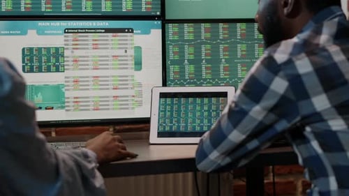 Two people analyzing financial data on monitors