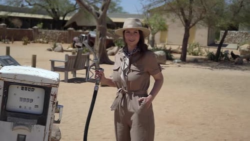 Woman in Overalls and Hat Picks Up Filling Pistol at Old Abandoned Gas Station