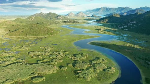 Bends and curves of blue river flowing through green valley toward distant mountains.
