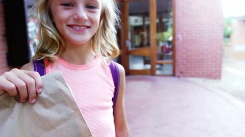 Portrait of happy schoolgirl holding paper bag in campus at school