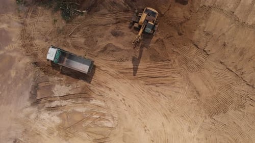 Aerial top view: yellow excavator pouring soil into tipper.