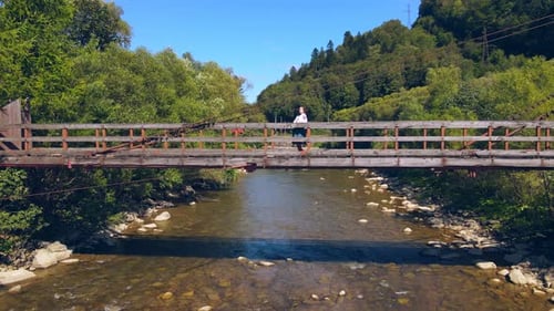 Aerial View From Old Wooden Suspension Bridge Over a Mountain River. Girl Standing on a Wooden