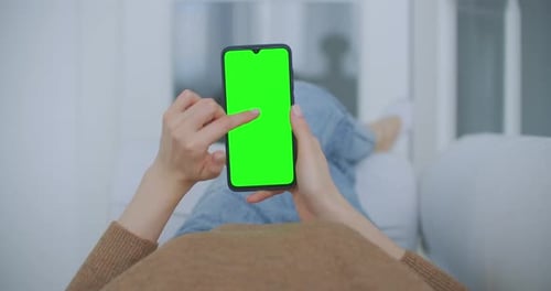 Point of View of Woman at Modern Room Sitting on a Chair Using Phone With Green Mock-up Screen