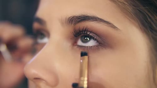 Vue rapprochée des mains d'un maquilleur professionnel utilisant un pinceau de maquillage pour appliquer des ombres à paupières