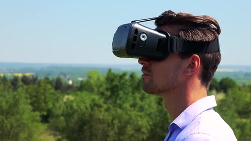Jovem bonito usa óculos de realidade virtual - campo ao fundo - closeup da cabeça