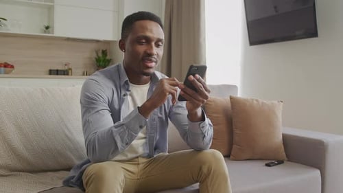 Young Adult Africanamerican Man Browsing on His Smartphone in His Apartment