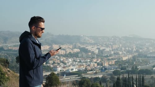 Man Uses Phone with City View